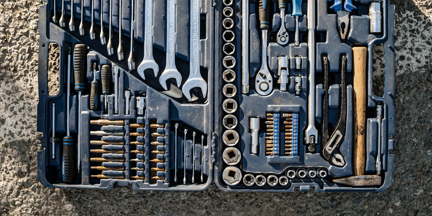An open toolbox seen from above on a concrete floor, with rows of spanners, sockets, screwdrivers, pliers and a hammer in their slots.